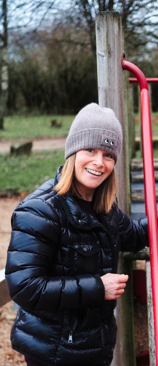 Suzanne smiling outdoors, wearing a grey hat and a dark jacket